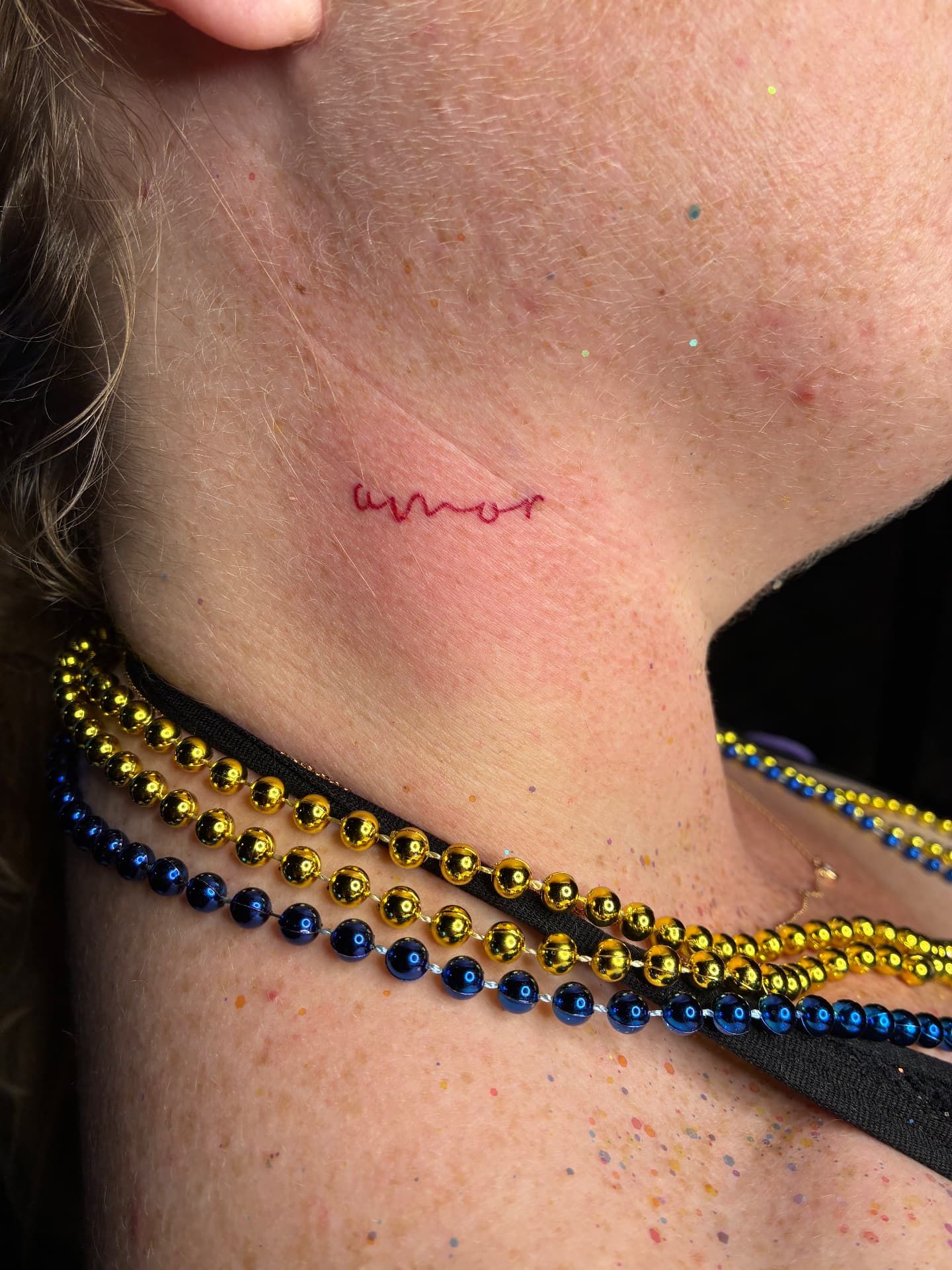 Red ink 'amor' script neck tattoo